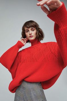 Woman in a red turtleneck sweater and plaid skirt posing in a studio