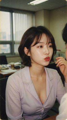 Woman with short hair and red lipstick in a light purple shirt in an office