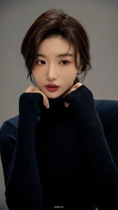 Woman in a dark turtleneck with hands near her chin, looking away