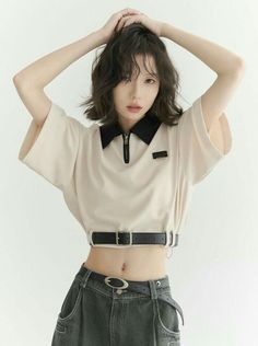 Woman with short hair wearing a crop top and jeans with hands on head