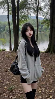 Woman with long black hair wearing a grey hoodie and black shorts in a forest by a lake
