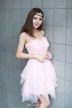 Woman in a pink strapless dress and headband standing against a tiled wall