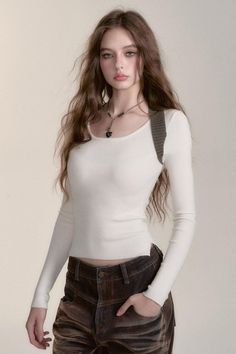 Woman with long hair wearing a white top and brown pants with a heart necklace