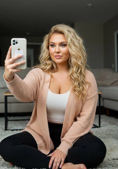 Woman with blonde curly hair taking a selfie while sitting on a rug