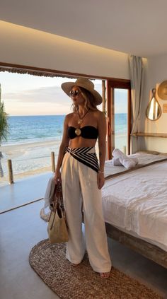 Woman in a straw hat and bandeau top looking out at the beach from indoors