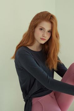 Woman with long red hair and freckles wearing a dark long sleeve shirt and pink leggings