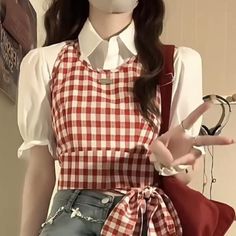 Person in a red gingham crop top and white shirt making a peace sign