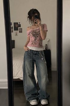 Person in baggy jeans and a pink top taking a mirror selfie indoors