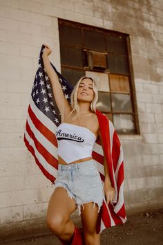 Woman with blonde hair holding an American flag, wearing a crop top and denim shorts
