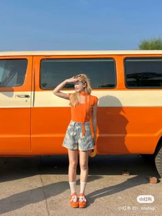 Woman in an orange top and denim shorts standing next to an orange van