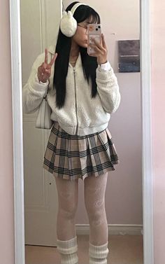 Person in a white jacket and plaid skirt taking a mirror selfie