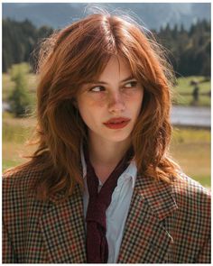 Woman with red hair and freckles wearing a plaid jacket and red scarf outdoors