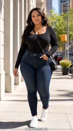 Woman with long dark hair in a black top and blue jeans walking on a city street
