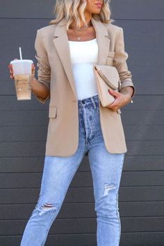 Woman in a beige blazer and ripped jeans holding iced coffee and a clutch bag