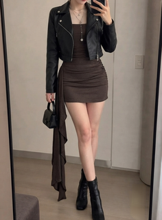 Woman in a black leather jacket and brown mini dress holding a black handbag