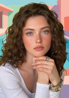Woman with curly hair and light eyes wearing a white top and jewelry
