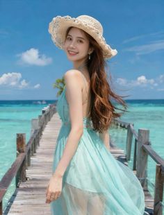 Woman in a light blue dress and straw hat on a wooden pier over tropical water