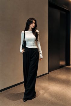 Woman with long dark hair in a white top and black pants indoors