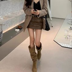 Person in a brown blazer and mini skirt with knee-high boots indoors