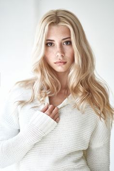 Blonde woman with freckles wearing a white sweater, looking directly at the camera