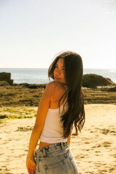 Woman with long dark hair on a beach at golden hour, looking over her shoulder