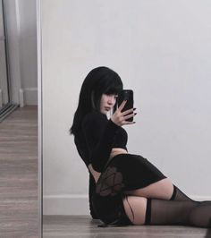Woman with black hair in a black top and mini skirt taking a mirror selfie