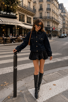 Woman in a denim jacket and mini skirt on a city street with a cafe in the background