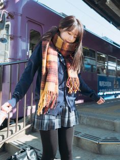 Young woman in a school uniform and plaid scarf at a train station