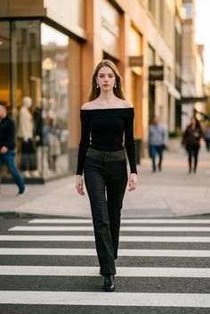 Woman in a black off-shoulder top and dark pants walking on a city crosswalk