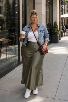 Woman in a denim jacket and long skirt holding a coffee cup on a city street