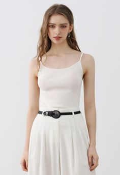 Woman with long hair wearing a white tank top and white pants with a black belt