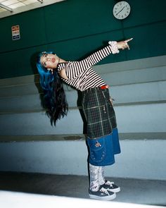 Woman with blue hair in a striped shirt and plaid skirt posing indoors