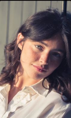 Woman with freckles and long hair in a white shirt, lit by golden hour sun