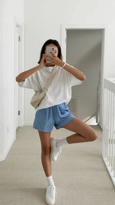Woman in a white t-shirt and striped shorts taking a mirror selfie indoors