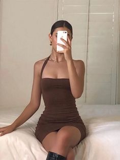 Woman in a brown halter neck dress taking a mirror selfie while sitting