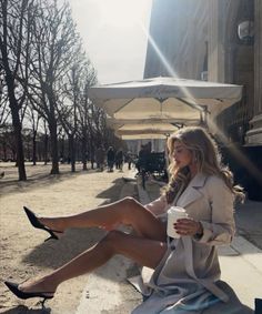 Woman in a trench coat and high heels sitting outdoors at a cafe