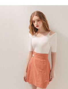 Woman with long hair wearing a white top and orange skirt indoors