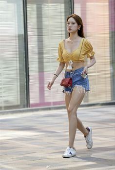 Woman in a yellow crop top and denim shorts walking on a street