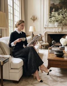 Woman in a black collared shirt and long skirt reading a magazine in a living room