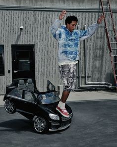 Man in a blue hoodie and camo shorts balancing on a toy car
