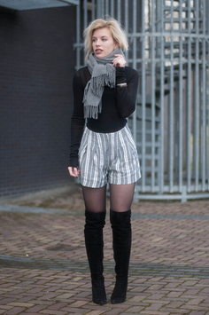 Woman with blonde hair wearing a gray scarf, striped shorts, and thigh-high boots