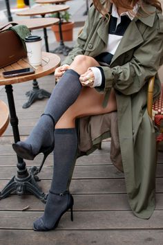 Woman in a trench coat and knee-high socks sitting at an outdoor cafe