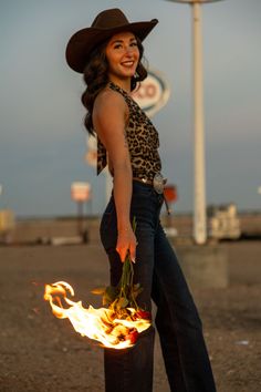 Woman in a cowboy hat and leopard print top holding burning roses outdoors