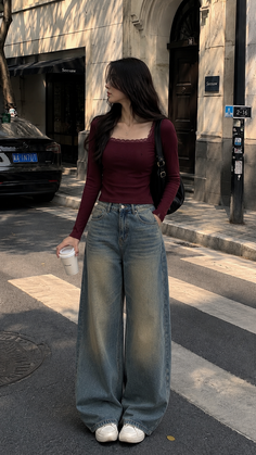Woman in a maroon top and wide leg jeans standing on a street with a coffee cup