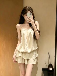 Woman in a beige top and ruffled skirt taking a mirror selfie