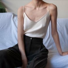 Person in a light top and dark pants sitting indoors with soft lighting