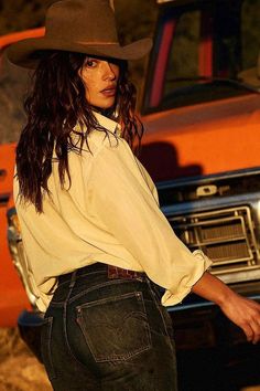 Woman in a cowboy hat and jeans looking over her shoulder at golden hour