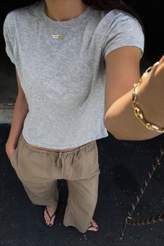 Person in a gray t-shirt and khaki pants with a gold necklace and bracelet
