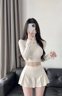 Woman in a crop top and pleated skirt taking a mirror selfie