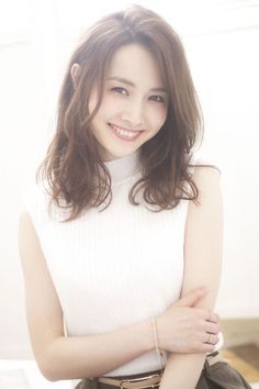 Woman with long wavy hair wearing a white sleeveless top, smiling at the camera